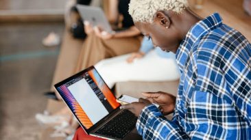 Person in a plaid shirt using a laptop and smartphone