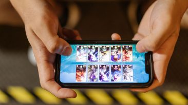Hands holding a smartphone horizontally while playing a mobile card game on the touchscreen